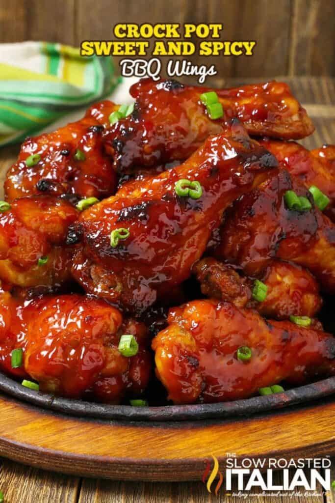 sweet and spicey BBQ wings with green onion slices on a cast iron plate sitting on a wood surface.