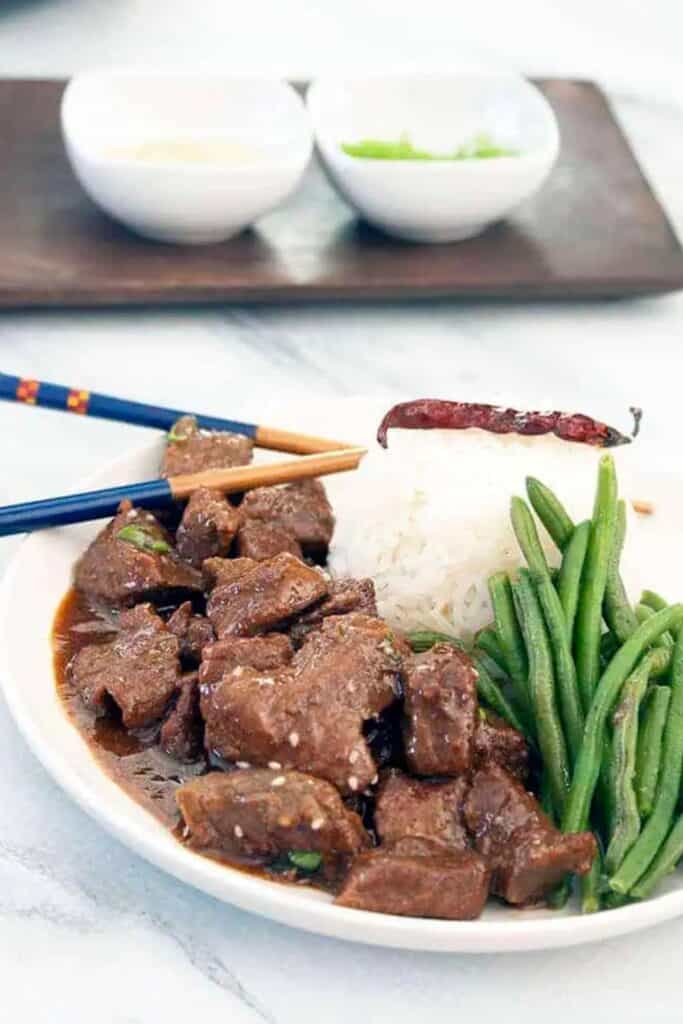 slow cooker korean beef on a white plate with green beans, rice, and a chili pepper.