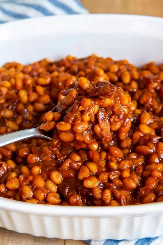 Baked beans in a white dish with a silver spoon.