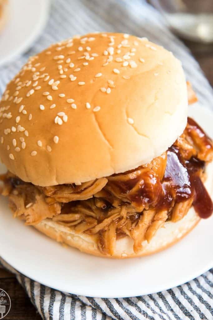 slow cooker barbeque chicken on a sesame bun on a white plate.
