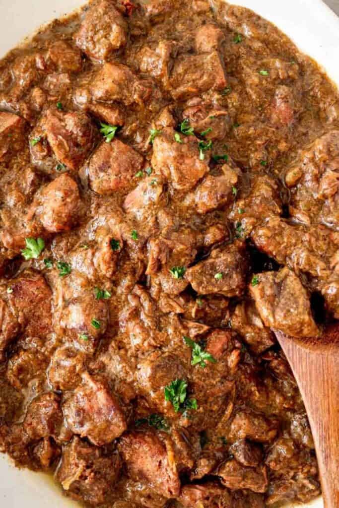 slow cooker garlic steak bites with a wooden spoon and parsley.