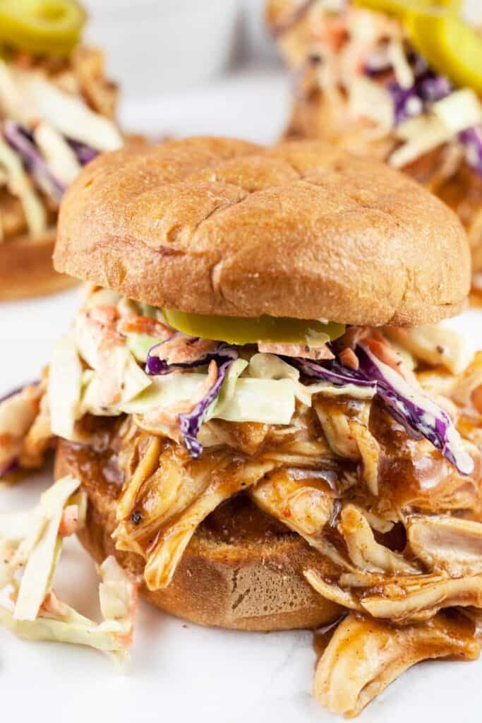 BBQ chicken sandwiches on a bun with cole slaw and pickles.