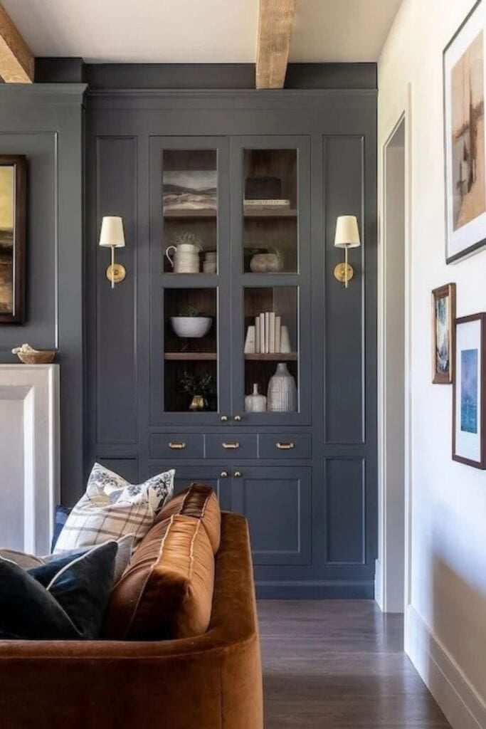 Built-ins pianted a muted dark blue with two sconces and a dark orange velvet sofa.