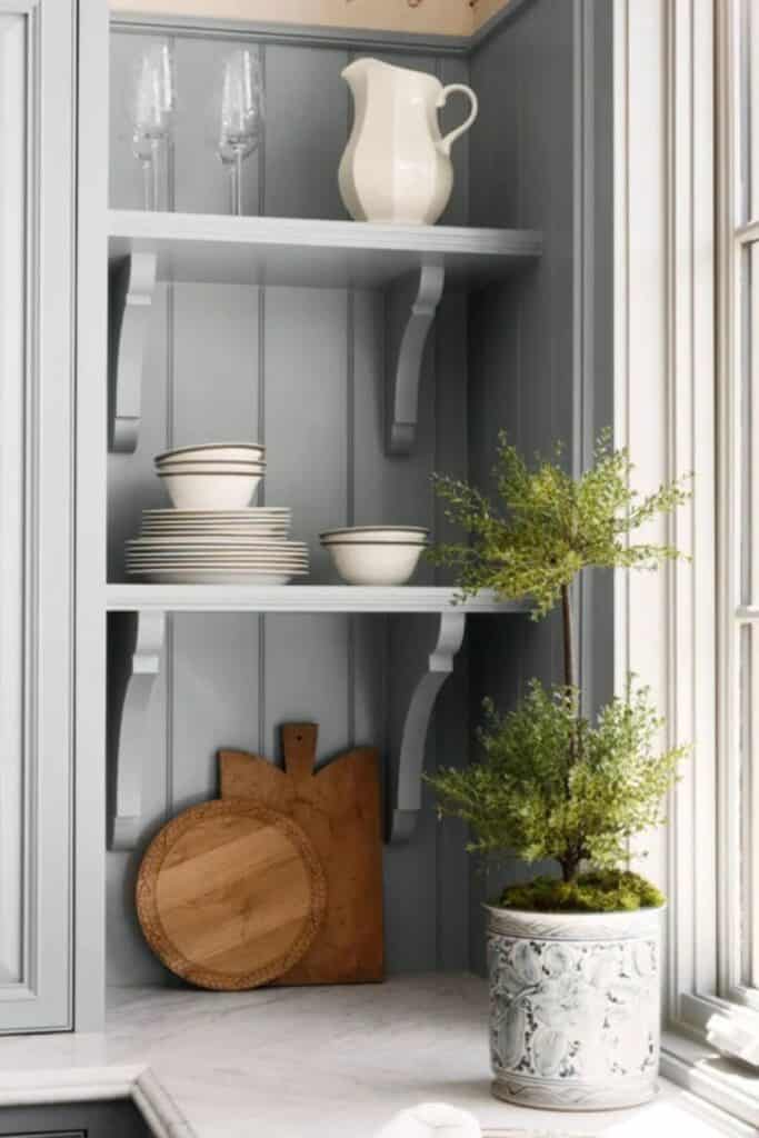 Ope n shelving with cuttingboards and dishes being displayed with a plant and on the perpendicular wall are windows.