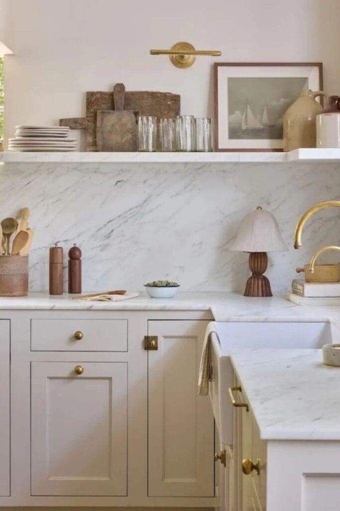 a kitchen with cream cabinets, a farmhouse sink, gold hardware and open shelving.