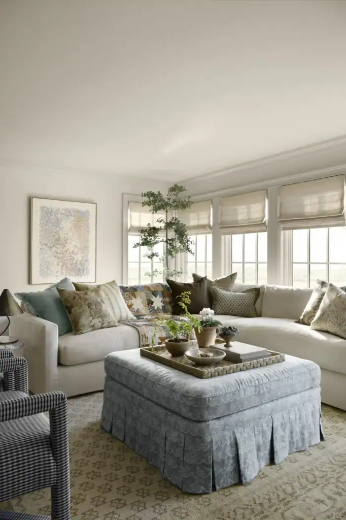 A family room with a secontional and a skirted ottoman with a tray of acessories.